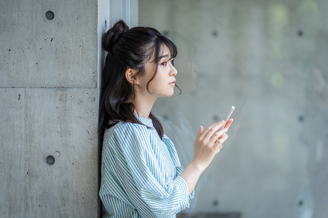 スマホを持って壁にもたれかかる若い女性