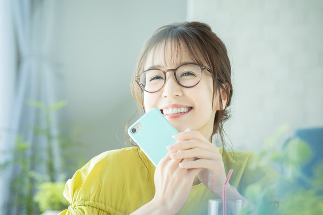 スマホを持って笑うメガネの若い女性