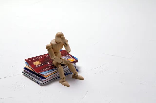 クレジットカードの山に座って頭を抱える人形