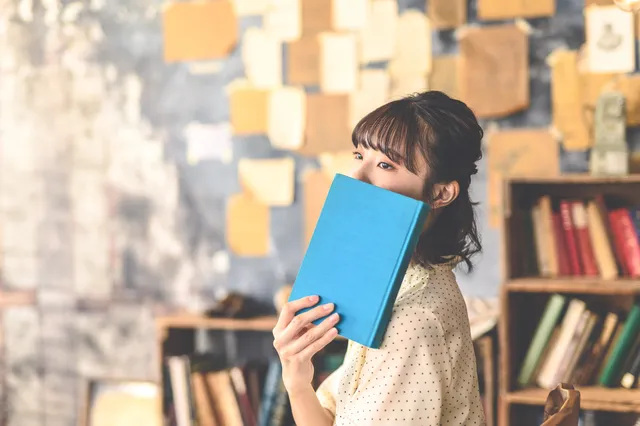 本で顔を隠す女性